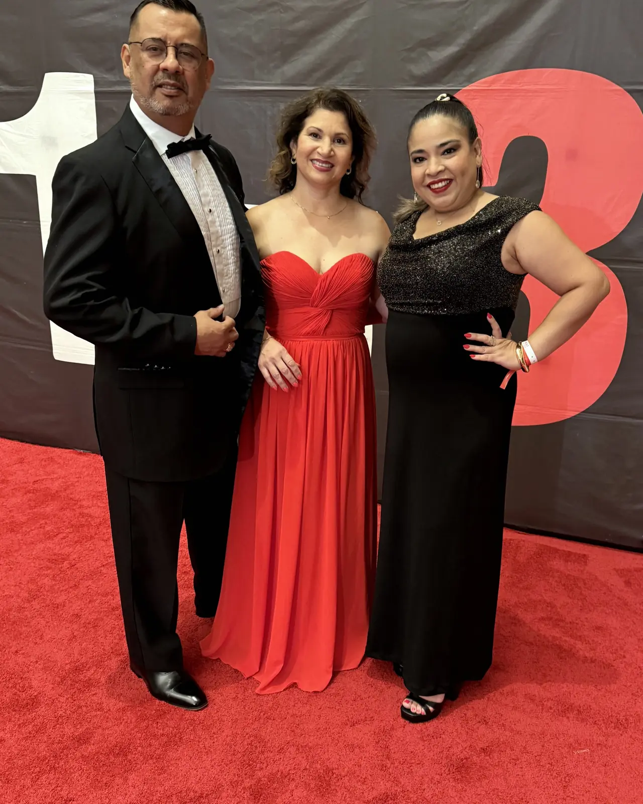 Un integrante de smoking y dos integrantes de vestido largo posan en la alfombra roja de la gala del MAS en Miami